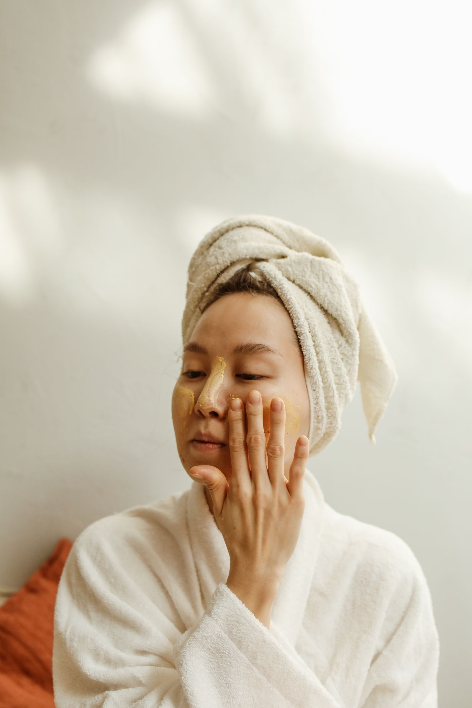 A woman calmly applying skincare with a towel wrapped around her hair