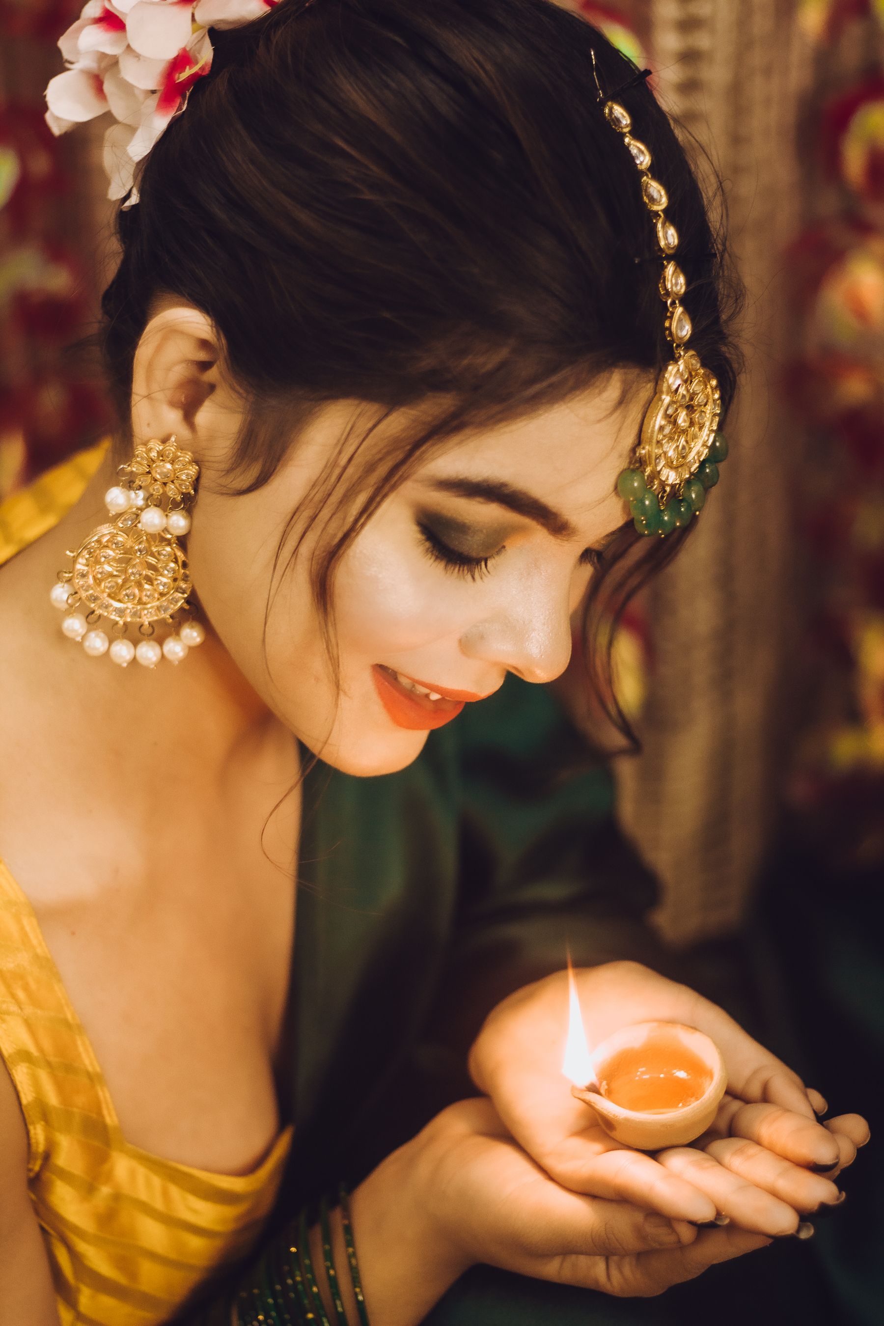 Indian woman in festive jewellery and traditional attire holding a glowing diya