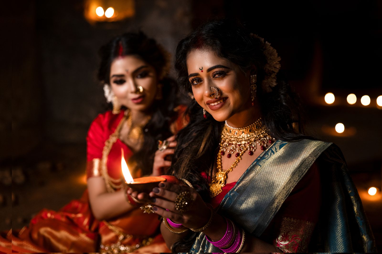 Two Indian women dressed for a festival holding a glowing diya