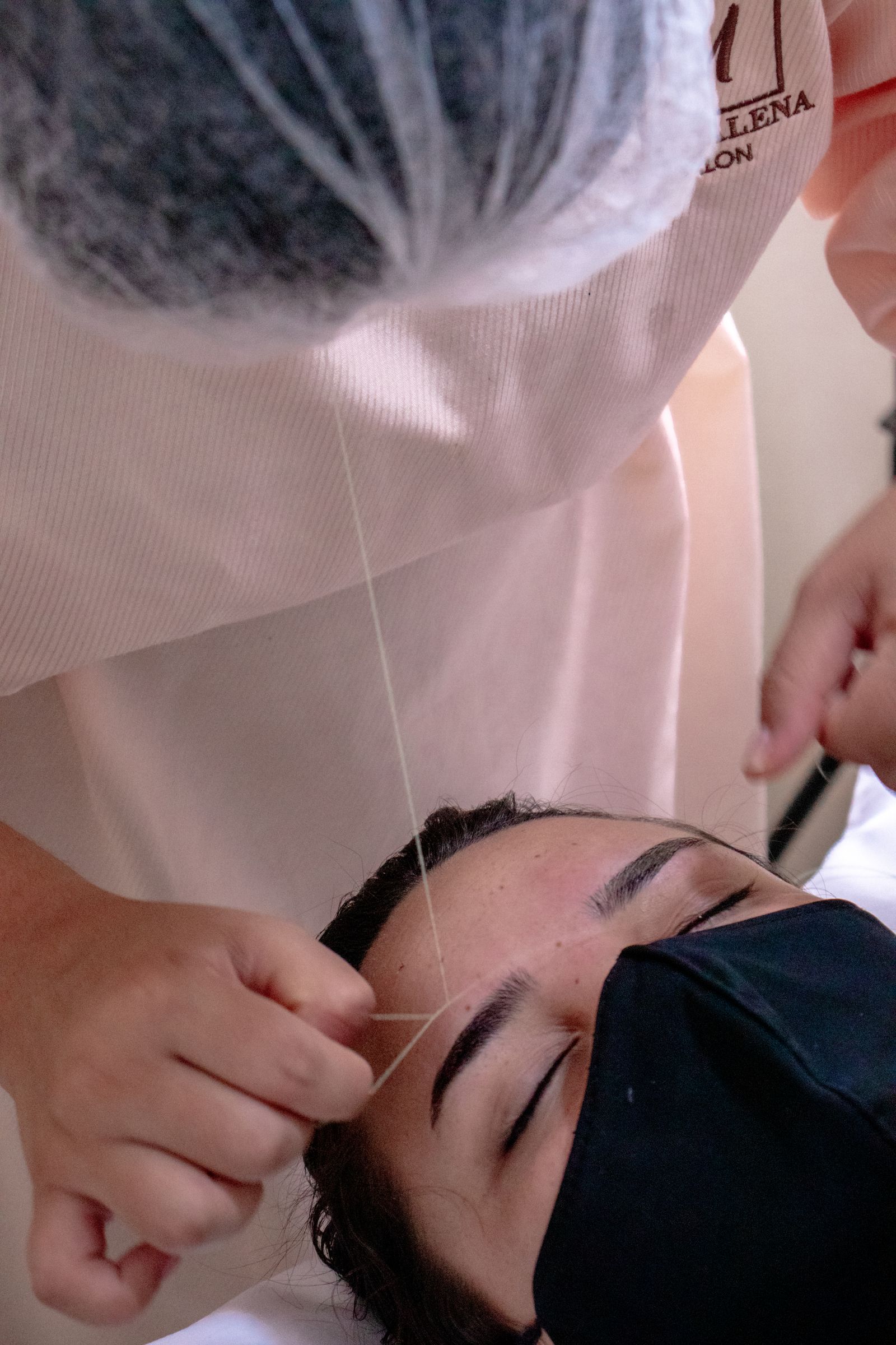 A beauty professional shaping eyebrows with threading
